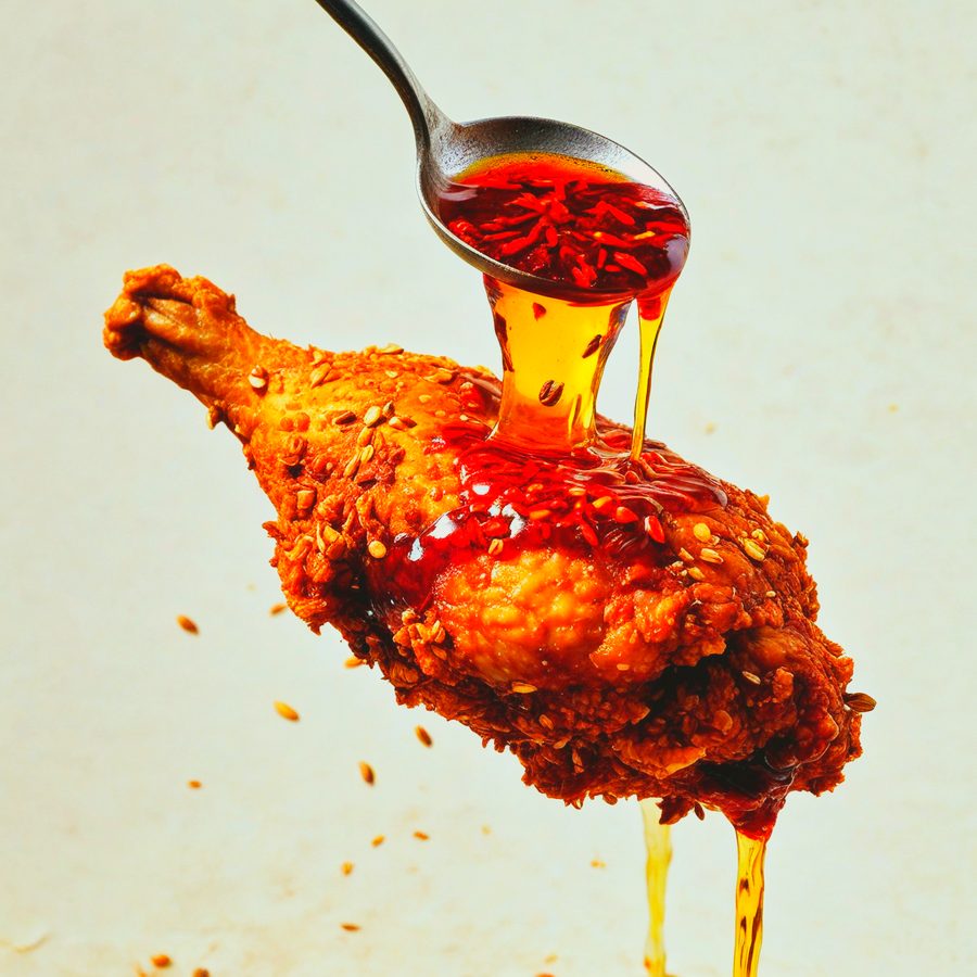 Red chilli oil with visible flakes and seeds being spooned over fried chicken